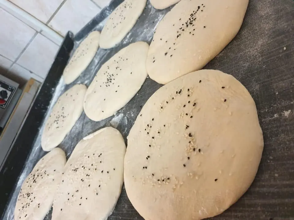 Frisch vorbereitete Fladenbrot-Teiglinge mit Sesam und Schwarzkümmel auf dem Backblech in der Küche von Ali's Restaurant