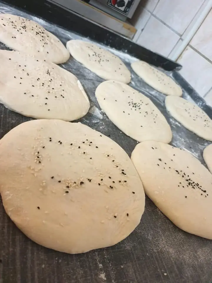 Frisch vorbereitete Fladenbrot-Teiglinge mit Sesam und Schwarzkümmel auf dem Backblech in der Küche von Ali's Restaurant